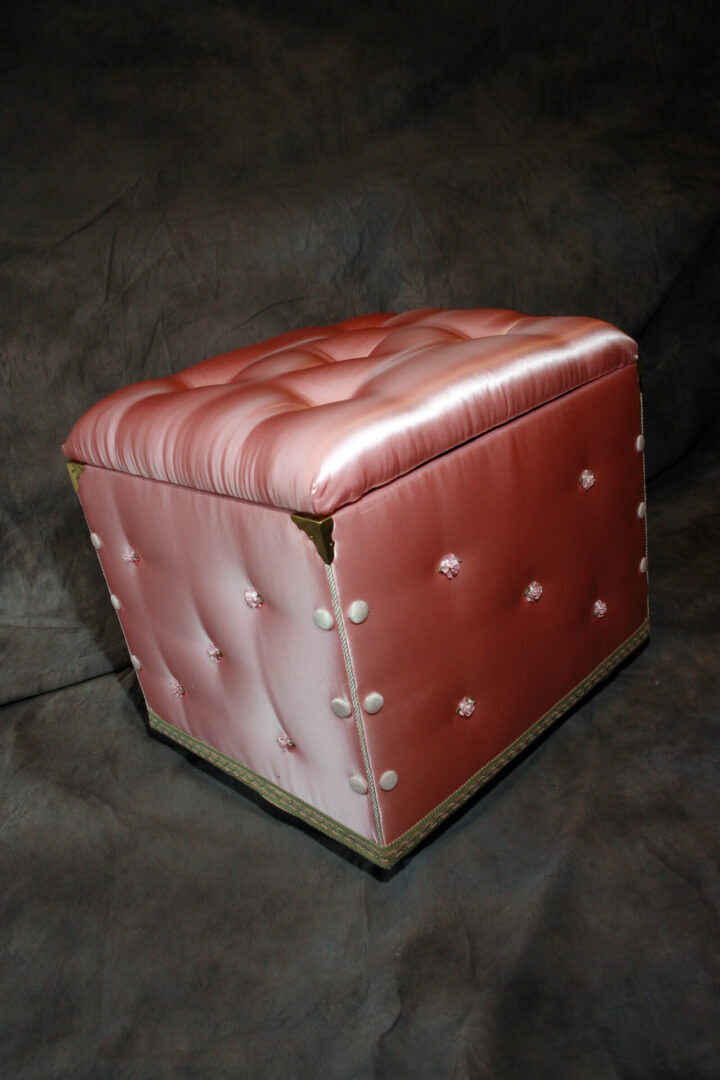 Pink tufted ottoman on dark background.