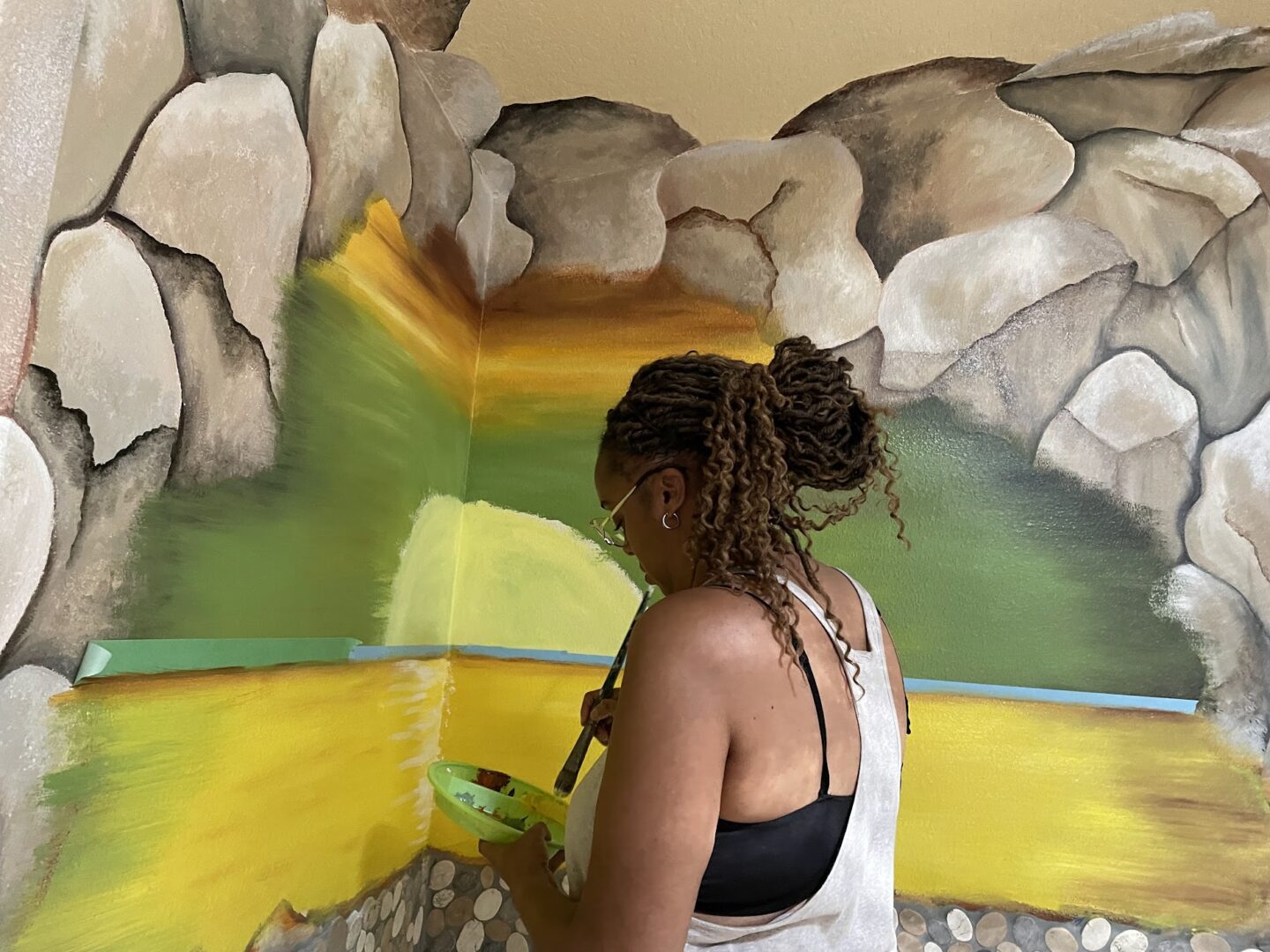 Woman painting mural with rocks and greenery.